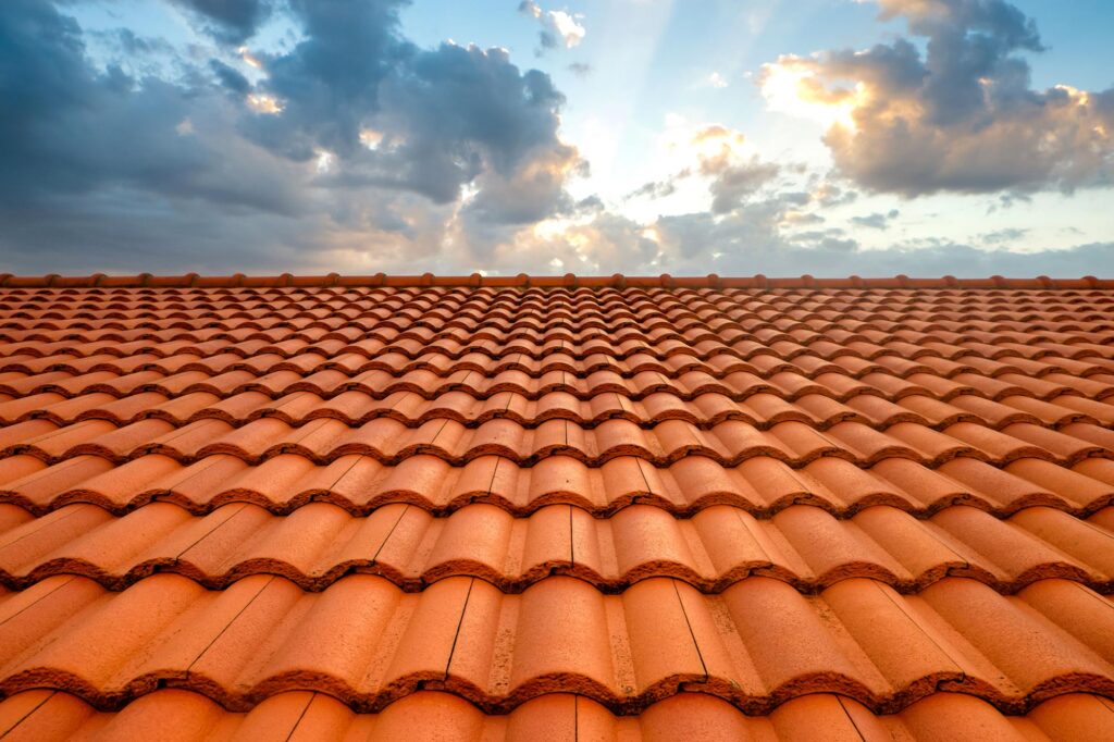 A red terracotta tiled roof extending toward the horizon under a partly cloudy sky with sunlight breaking through the clouds.